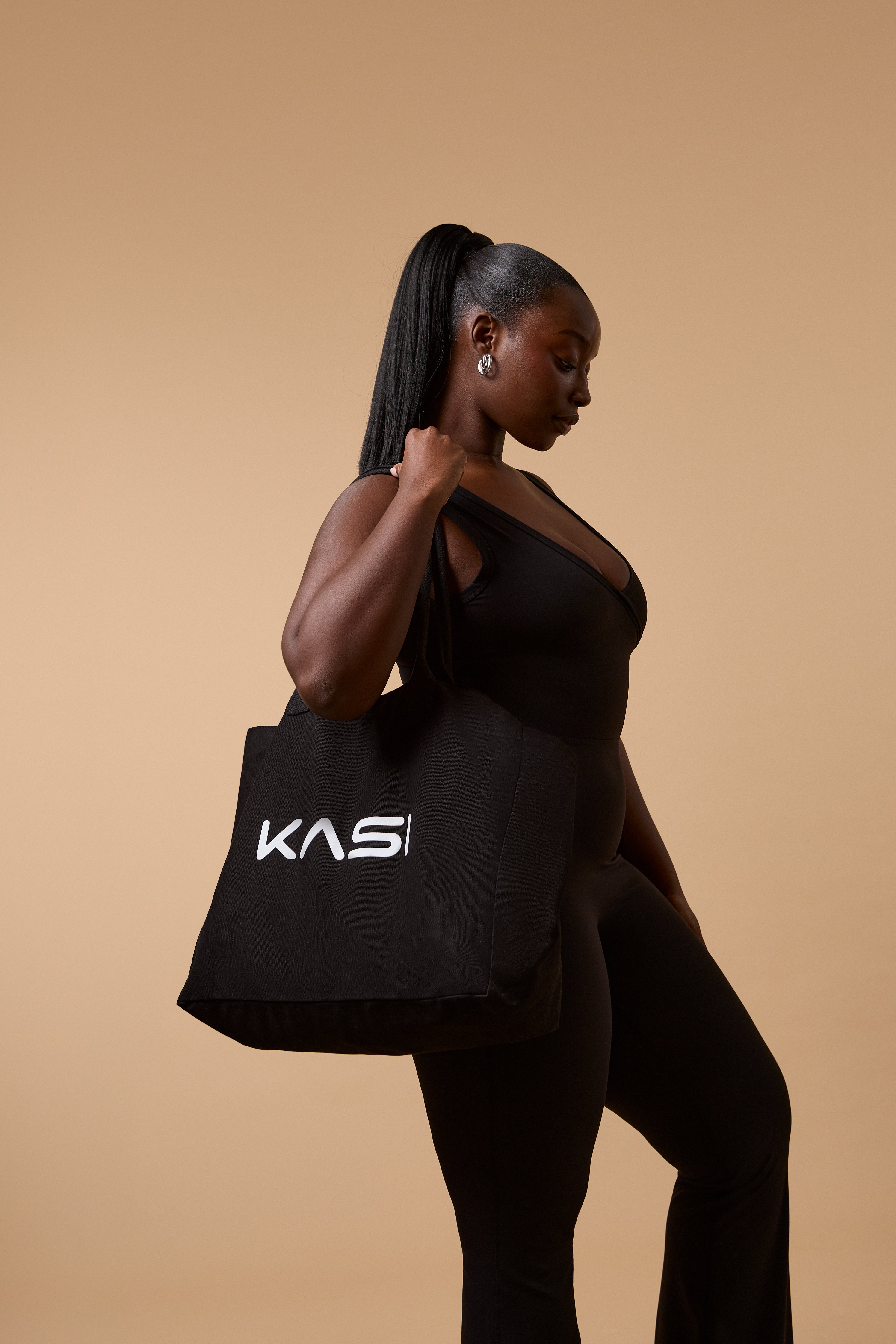 Woman holding a black tote bag with 'KAS' logo against a beige background