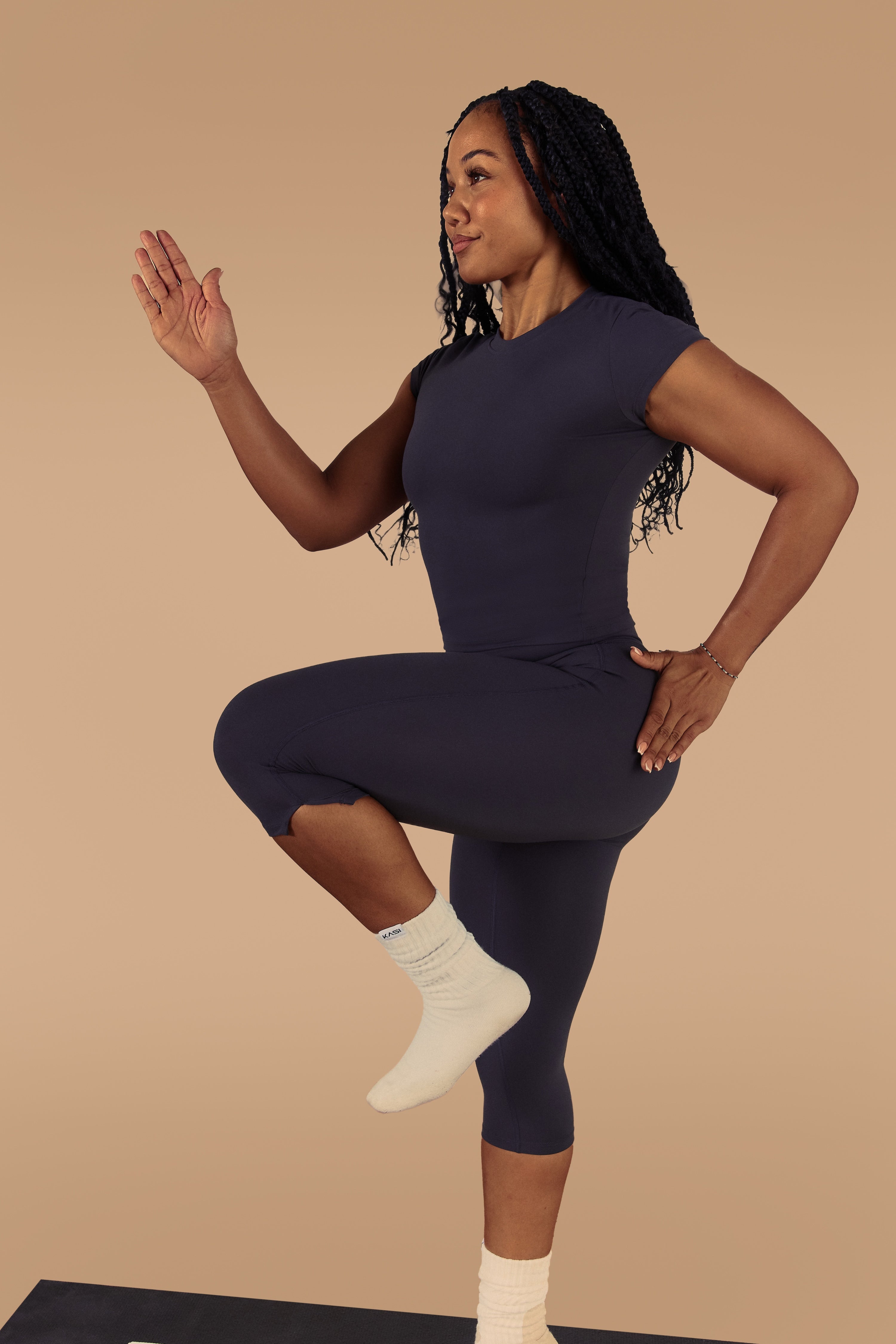 Person in a navy blue outfit performing a yoga pose on a beige background