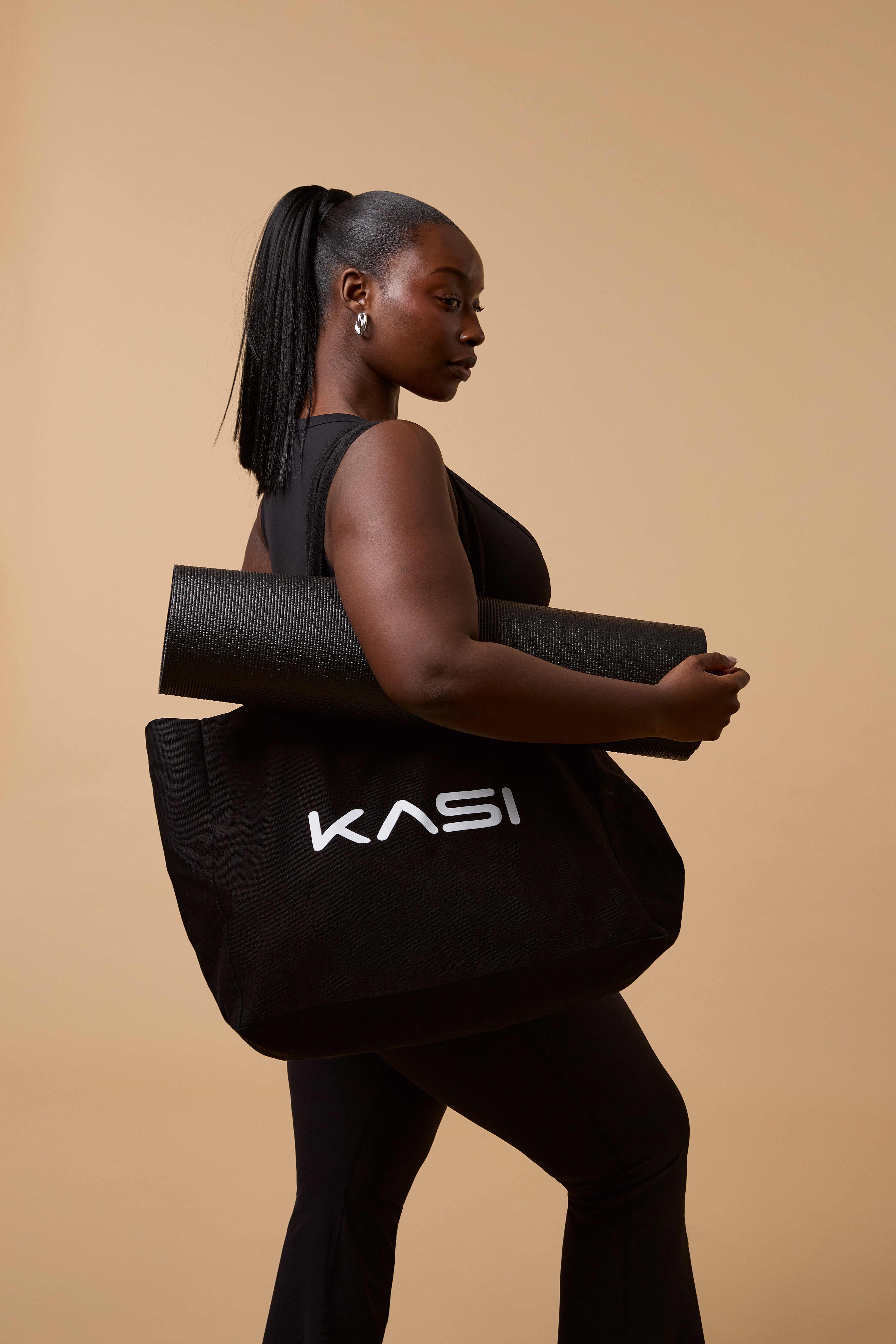 Woman holding a black KASI yoga mat bag against a beige background