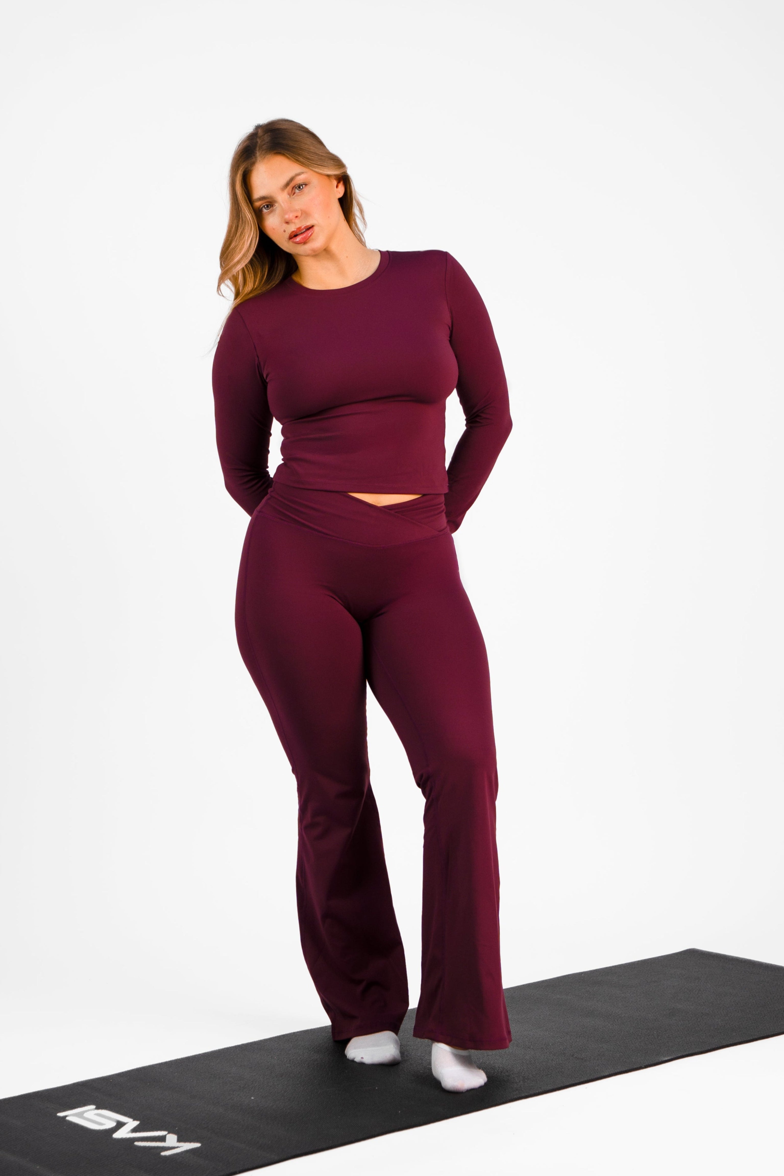 Woman in burgundy athletic wear standing on a black mat against a white background