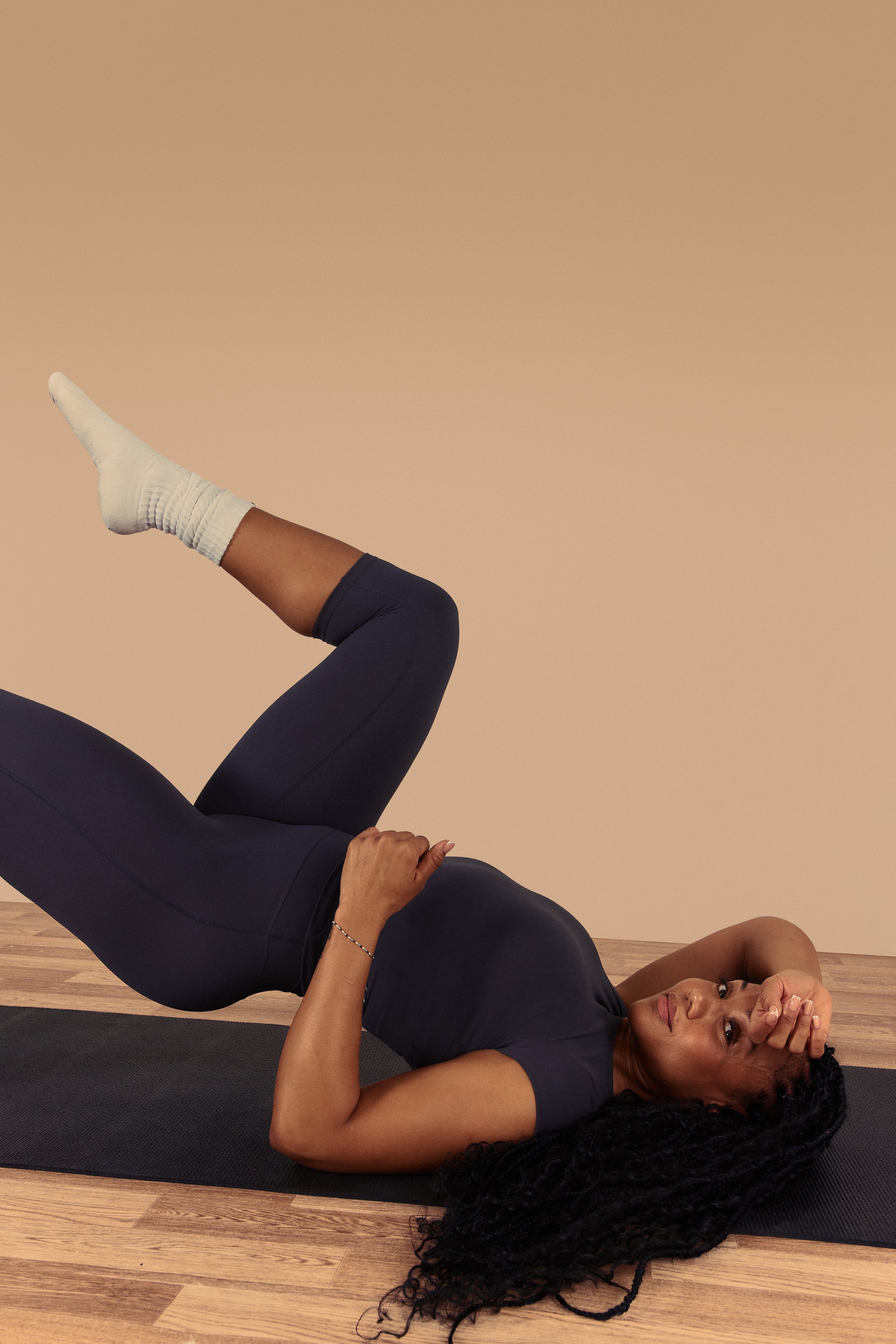 Woman in dark blue athletic wear lying on a mat against a beige wall.
